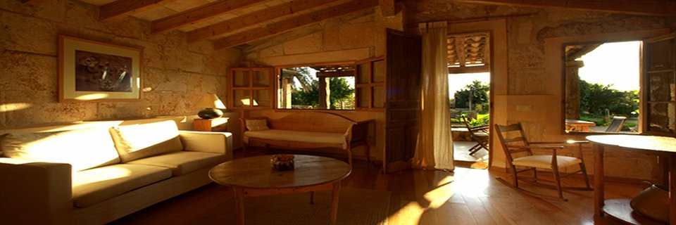 A sitting room at Sant Blai, beamed ceiling and stone walls, sofas around a low table, doors open to the garden