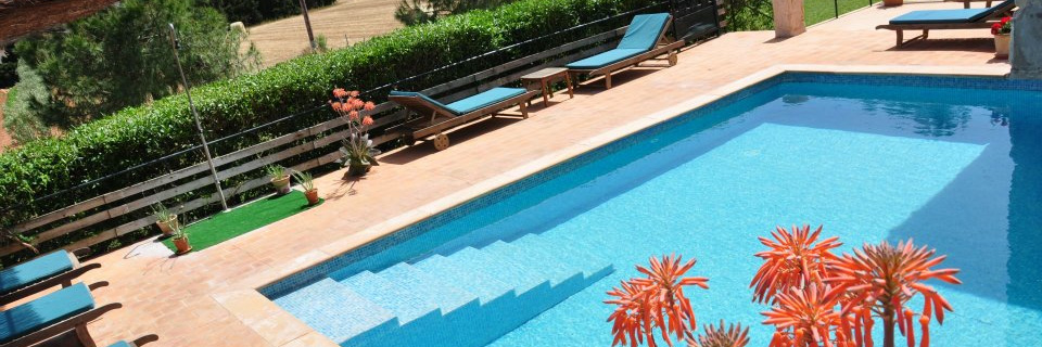 The pool at Sant Blai above the Campos plain, terracotta deck and loungers, aloe in flower, farmland running to the hills